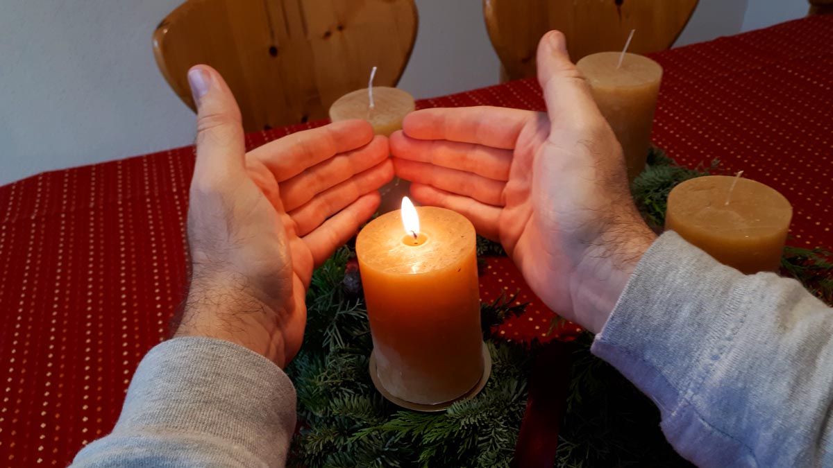 Beleuchtete Hände um Adventskranzkerze